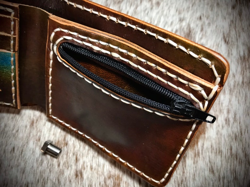 May include: A brown leather wallet with a zippered pocket and white stitching. The wallet is open and the zipper is pulled down to reveal the pocket.