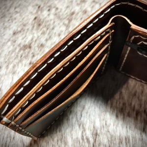May include: A brown leather wallet with white stitching and multiple card slots. The wallet is open to reveal a zippered pocket.