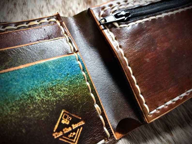 May include: A brown leather wallet with a zippered pocket and multiple card slots. The wallet has white stitching and a logo that reads "The Shoe Room".