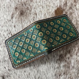 May include: A green leather wallet with a gold and green patterned design. The wallet has a white stitch around the edges.