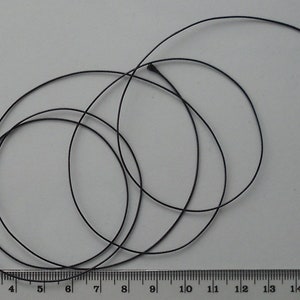 May include: A close-up of a black cord or string, approximately 20 cm long, coiled on a white surface with a ruler for scale.