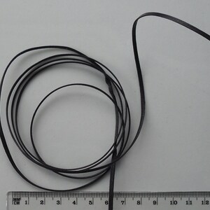 May include: A close-up of a black satin ribbon wound into a coil. The ribbon is approximately 15 cm long.