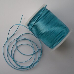 May include: A spool of light blue leather cord. The cord is wound around a white plastic spool.