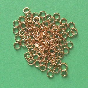 May include: A large pile of gold jump rings. The rings are small and round, and they are all linked together.
