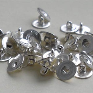 May include: A collection of silver snap buttons. Each button features a flat, circular base with a loop for sewing and a domed top that fastens to the base. The buttons are made of a shiny metal.