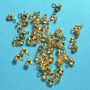 May include: A pile of gold-coloured metal bead caps with a loop on each side. The caps are designed to be used for jewellery making.