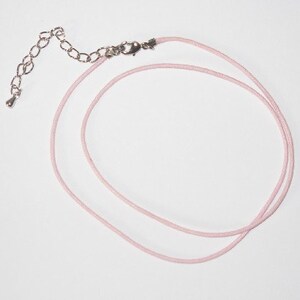 May include: A pale pink necklace with a silver-coloured chain and clasp. The necklace cord is a thin, round material. The chain has an adjustable length.
