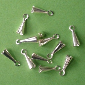 May include: A group of silver-toned metal cord end caps with a pointed tip and a small loop at the top. The caps are arranged on a green surface.