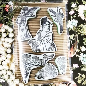 May include: A set of rubber stamps featuring Japanese-inspired designs. The stamps include images of women in traditional attire, birds, and floral patterns. The stamps are packaged in a clear plastic sleeve with the text "Sweet Manhattan Stamps".