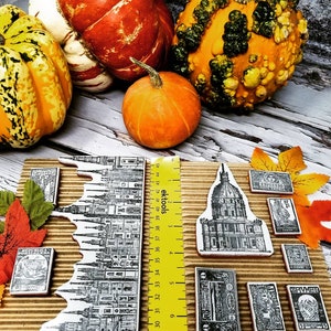 Puede incluir: Una colecci&oacute;n de sellos postales antiguos con ilustraciones en blanco y negro de edificios y otros dise&ntilde;os. Los sellos est&aacute;n dispuestos sobre una superficie de cart&oacute;n marr&oacute;n con una regla amarilla y varias calabazas.