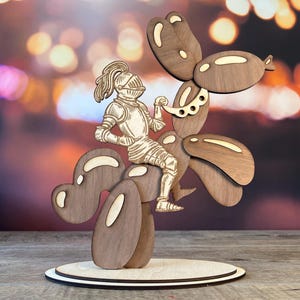 May include: A laser-cut wooden sculpture featuring a knight in full plate armor riding a balloon animal dog. The knight is light-colored wood, while the balloon dog is dark brown wood with lighter wood accents on the balloon segments.