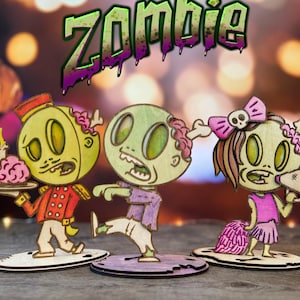 May include: Wooden zombie figurines with a cartoonish design. One zombie holds a tray with a cake, another is mid-step, and the third is a cheerleader with a megaphone. The word "Zombie" is written above the figurines.