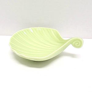 May include: A light green ceramic dish shaped like a leaf with a curled edge. The dish has a ribbed texture.