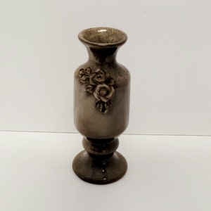 May include: A small, brown ceramic vase with a floral design. The vase has a wide base and a narrow neck.