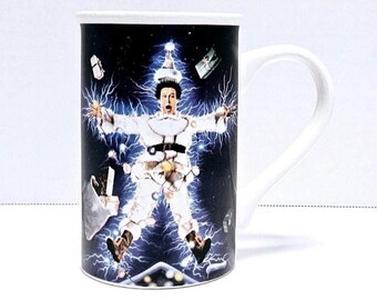 May include: White ceramic mug with a black and blue image of a man dressed in a white suit with Christmas lights wrapped around him. The man is surrounded by lightning bolts and presents. The mug has a white handle.