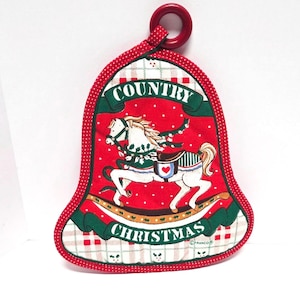 May include: Bell-shaped Christmas potholder with a red background and a white rocking horse design. The words "COUNTRY CHRISTMAS" are printed on the potholder. The potholder has a red handle.