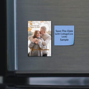 May include: A rectangular save-the-date magnet featuring a photograph of two people embracing, framed by a decorative border. The text reads Save the Date June 12, 2027 and Kevin & Susanne. Beside it is a blue square sticky note with black text.