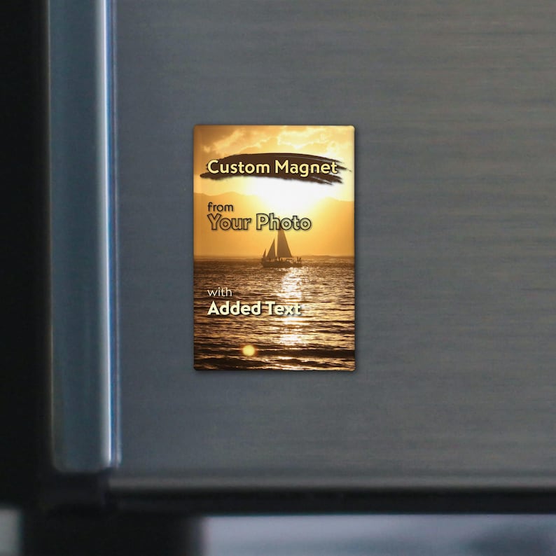 May include: A rectangular custom magnet featuring a sunset ocean scene with a sailboat silhouette. The text Custom Magnet from Your Photo with Added Text is printed in black and white over the golden horizon and shimmering water surface.