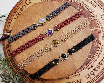 Könnte beinhalten: Vier geflochtene Armbänder mit verschiedenen farbigen Schnüren und Edelstein-Akzenten. Die Armbänder werden auf einem Holzkreis mit den Namen der acht Sabbate des Jahresrades am Rand angezeigt.