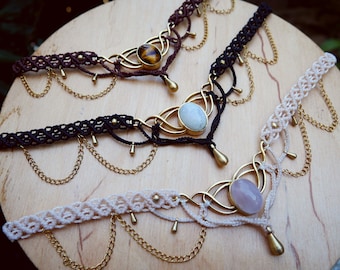 May include: Three macrame chokers with different colored stones and gold accents. The chokers are made with brown, black, and white cord and feature gold chains with teardrop-shaped charms.