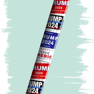 Pu&ograve; includere: Una penna nera e argentata con diversi adesivi rossi, bianchi e blu. Gli adesivi presentano il testo "Trump 2024" e "Save America".