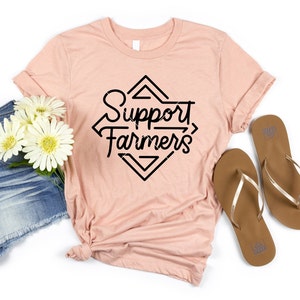 May include: A peach-colored t-shirt with a black graphic design that says "Support Farmers" in a diamond shape.