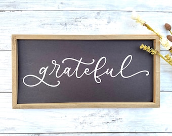 May include: A wooden framed sign with a dark grey background and the word "grateful" written in white cursive script.