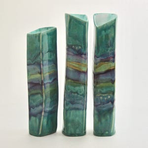 May include: Three ceramic vases with a teal and purple glaze. The vases are tall and slender with a rectangular shape.