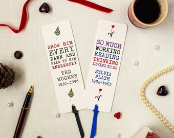 May include: Two white bookmarks with black and blue ribbon ties. The bookmarks feature quotes from Ted Hughes and Sylvia Plath. The left bookmark has a fern design and the right bookmark has a red flower design.