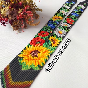 May include: A black beaded tie with a colorful floral pattern featuring sunflowers, poppies, and other wildflowers. The tie is handmade and has a unique, textured design.
