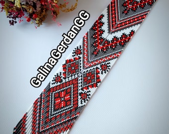 May include: A long, white beaded necklace with a geometric pattern in red and black. The necklace is made of small beads and has a fringe at the bottom. The text "GalinaGerdanGG" is written on the necklace.