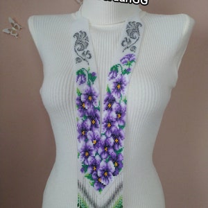Puede incluir: Un collar largo de cuentas con fondo blanco y flores moradas. El collar está hecho de cuentas pequeñas y tiene una franja en la parte inferior.