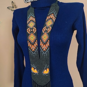 May include: A beaded necklace with a black base and geometric orange and yellow patterns. The necklace has a long, fringed bottom and the text "GalinaGerdanGG" in white.