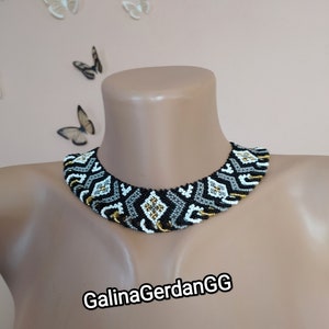 Peut inclure: Un collier ras de cou en perles noires, blanches et dorées avec un motif géométrique. Le collier est sur le cou d'un mannequin. Le texte "GalinaGerdanGG" est visible sous le collier.