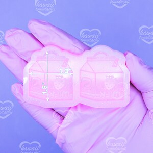 May include: A pink, glittery silicone mold featuring two milk carton designs with strawberry graphics. The mold measures 1.5 inches by 1.3 inches. The text "kawaii tomodachii" is visible on the image.