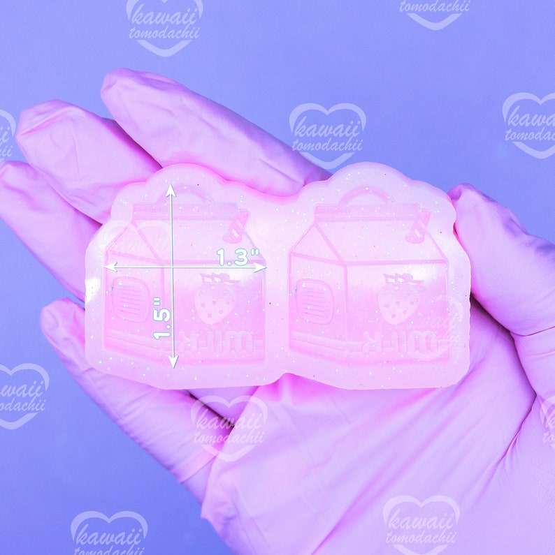 May include: A pink, glittery silicone mold featuring two milk carton designs with strawberry graphics. The mold measures 1.5 inches by 1.3 inches. The text "kawaii tomodachii" is visible on the image.
