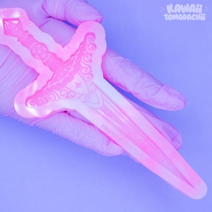 May include: A pink, glittery dagger-shaped mold with ornate details. The mold is held in a gloved hand against a purple background. The text "KAWAII TOMODACHI" is in the upper right corner.
