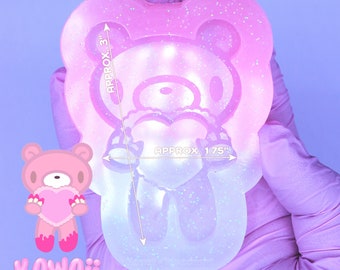 May include: A clear pink and white silicone mold of a kawaii bear holding a heart. The mold is approximately 3 inches tall and 1.75 inches wide. The mold is made of glitter-infused silicone.