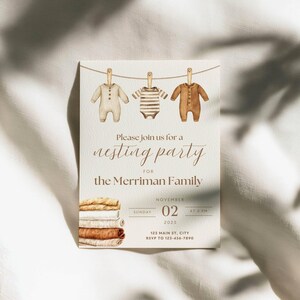 May include: A cream-colored invitation card featuring a watercolor illustration of three baby onesies hanging on a clothesline. Text reads: Please join us for a nesting party for the Merriman Family, Sunday, November 02, 2025, at 2 PM, 123 Main St, City.