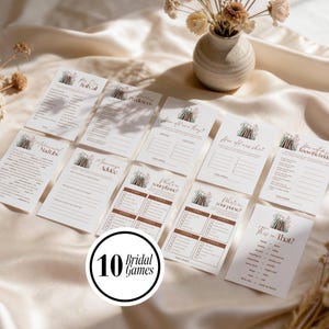May include: A set of ten white paper bridal game cards featuring a floral book illustration at the top. The cards include titles such as How Can Roll Call, Wedding Predictions, How Old Are They, How Old Was She, How Well Do You Know The Bride, Mad Libs, Marriage Advice, What's On Your Phone, What's In Your Purse, and This or That.