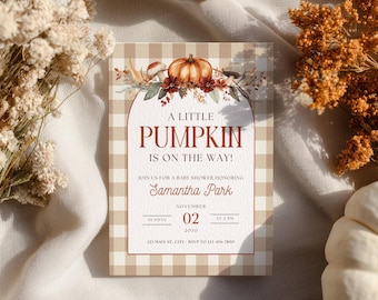 May include: A rectangular baby shower invitation card with a beige and white gingham border. The top features a watercolor illustration of a pumpkin, mushrooms, and autumn flowers. Text reads: A LITTLE PUMPKIN IS ON THE WAY! SAMANTHA PARK, NOVEMBER 02.