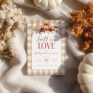 May include: A rectangular invitation card with a beige and white gingham pattern border. The center features an arched design with a pumpkin and floral illustration, text reading Fall in LOVE with Baby Merriman, November 02, 2030, and address details.