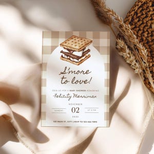 May include: A baby shower invitation with a watercolor illustration of a s'more. The invitation features the text "S'more to love!" and details for the event, including the date, time, and location. The background has a beige gingham pattern.