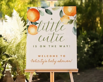 Puede incluir: Un letrero rectangular sobre un caballete de madera con ilustraciones en acuarela de naranjas y hojas verdes. El texto dice A little cutie IS ON THE WAY! WELCOME TO Felicity's baby shower! El fondo es de un color blanco hueso sólido.
