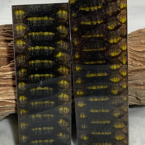 May include: Two rectangular pieces with a reptile skin pattern. The pattern features a dark brown base with yellow highlights, creating a textured appearance. The pieces are likely decorative or functional items.