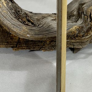 K&ouml;nnte beinhalten: Ein d&uuml;nnes, rechteckiges, helles Holzbrett mit einer glatten, flachen Oberfl&auml;che und einer dunklen, schmalen Kante, das vertikal vor einem St&uuml;ck verwittertem, strukturiertem Treibholz mit tiefen Rillen und brauner Oberfl&auml;che steht.