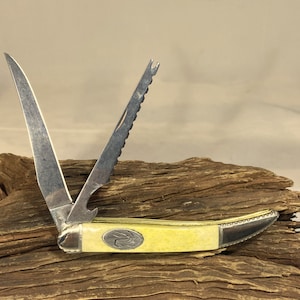 May include: A yellow handled pocket knife with a serrated blade and a bottle opener. The knife is open and the blade is pointing up.