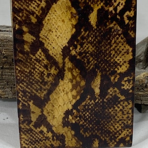 May include: A rectangular object featuring a high-gloss finish with a prominent dark brown and tan snakeskin pattern. The surface displays a detailed, repeating scale texture across the entire front face, creating a bold, naturalistic visual effect.