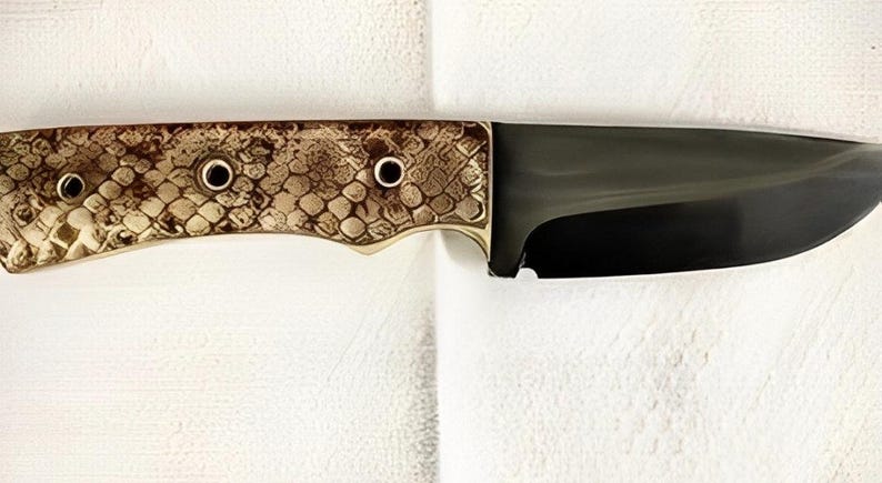 K&ouml;nnte beinhalten: Ein feststehendes Messer mit einer dunkel polierten Stahlklinge und einem Griff mit strukturiertem, hellbraunem und braunem Schlangenhautmuster. Der Griff ist mit drei kreisf&ouml;rmigen Metallnieten befestigt, die einen Kontrast zur Klinge bilden.