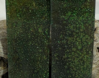 Op de afbeelding: Twee rechthoekige blokken met een donkergroen, getextureerd oppervlak. De blokken hebben een gespikkeld patroon met glinsterende groene glitter. De blokken staan naast elkaar en de achtergrond is licht.
